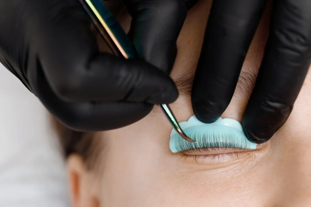 Close up of an eyelash tech wearing black gloves performing a lash extension procedure.