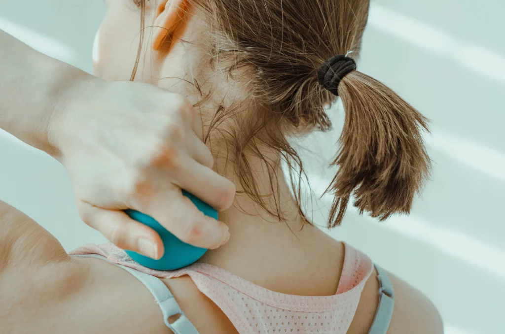 Close-up of a woman using a lacrosse ball to massage the back of her own neck.
