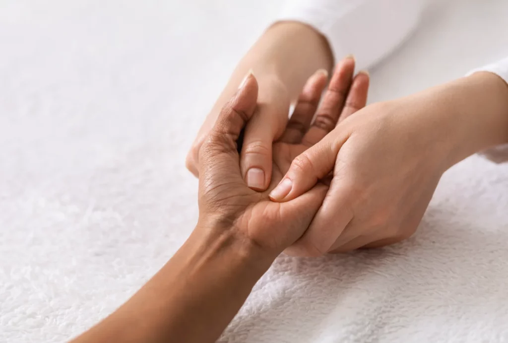 Close-up of a massage therapist gently massaging a client’s hand.