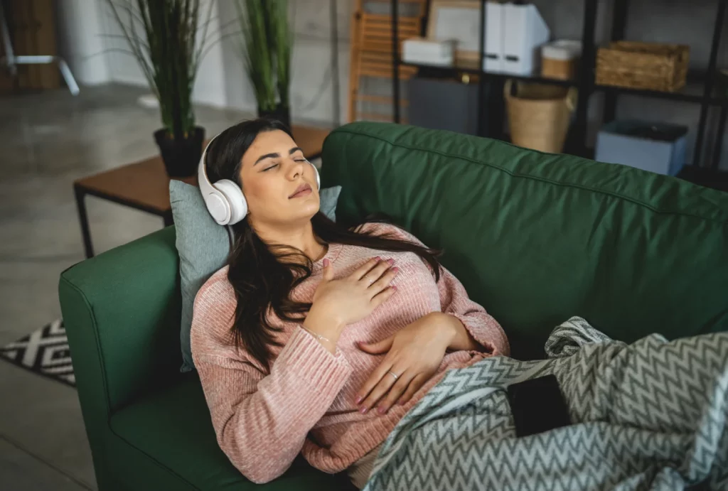 A woman lying on a couch with headphones on, resting peacefully with her eyes closed.