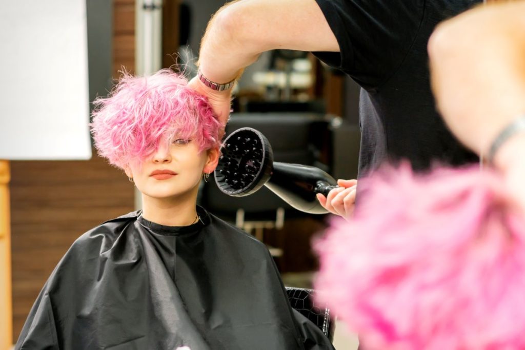 Hairstylist blow-drying client's pink hair
