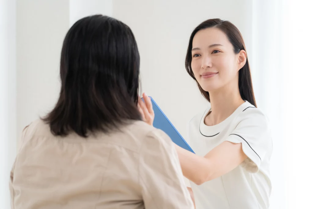 An esthetician checks a client's smile while holding a blue clipboard in a bright office space.