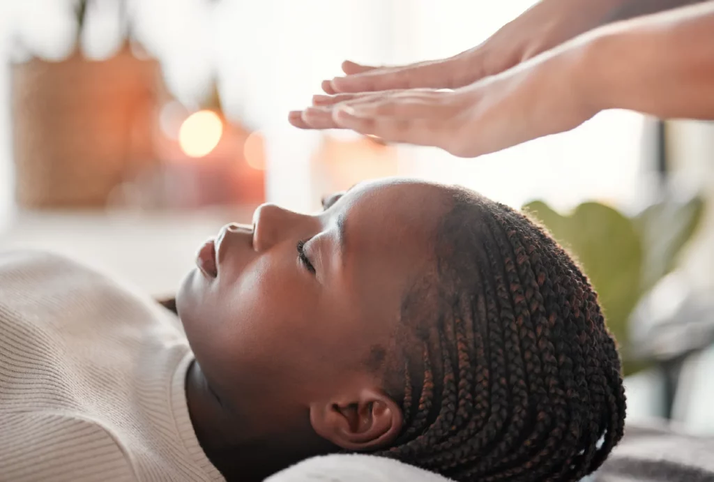 A client receives a Reiki treatment while lying down; the Reiki practitioner's hands hover above her head.