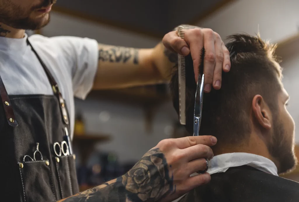 A barber cuts a client's hair using a comb and scissors.