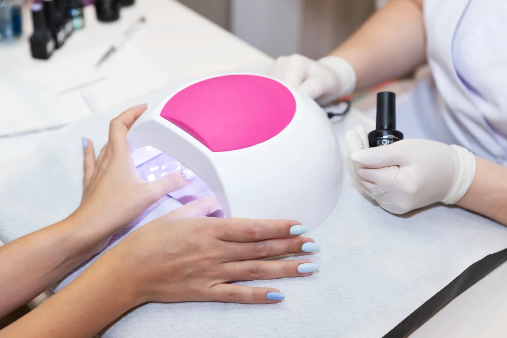 Close-up of a nail client drying their thumbs under a UV lamp during a manicure service.