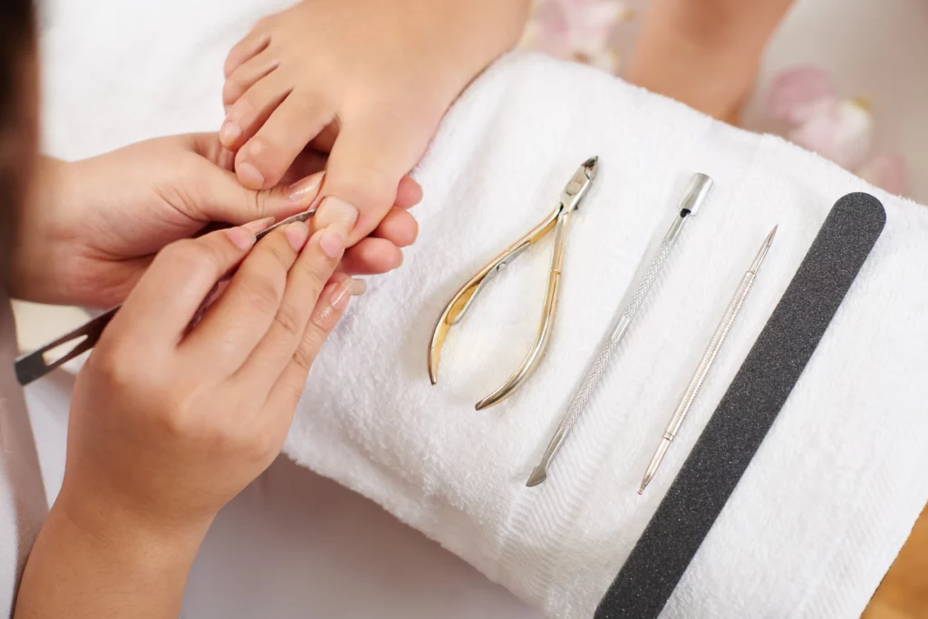 Close-up of a nail technician performing a pedicure with their tools laid out on a white towel.