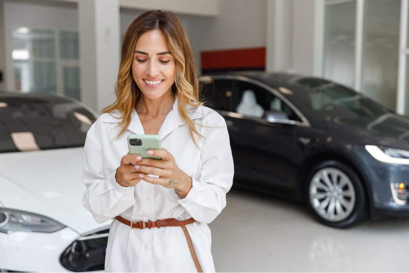 woman texting in front of some vehicles