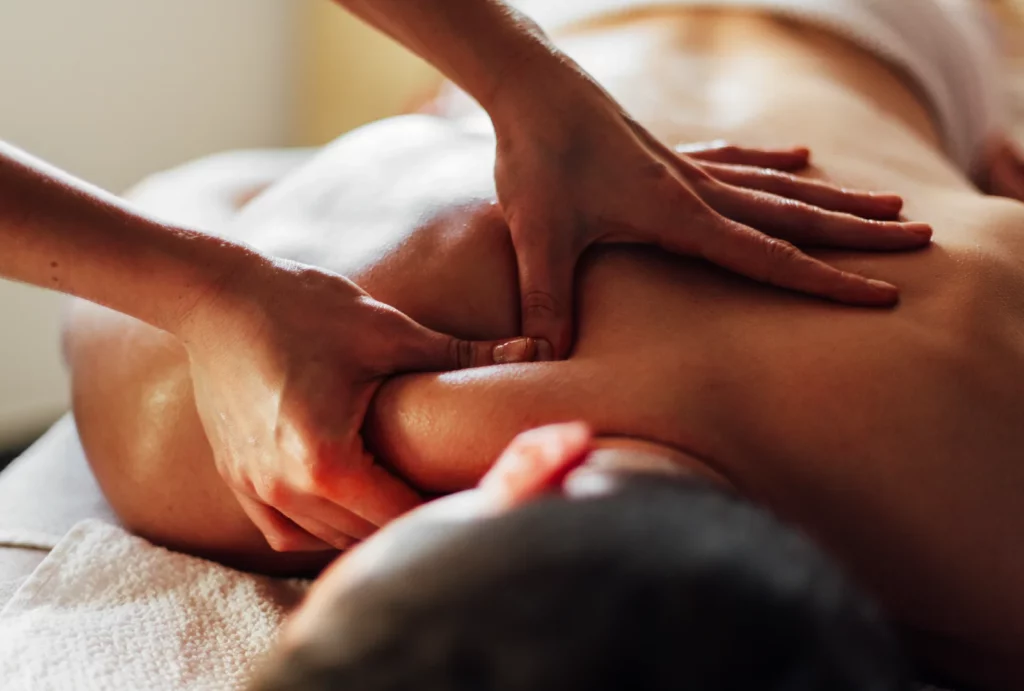 A close up of a massage therapist's hands performing a deep tissue massage on a client's neck and back.