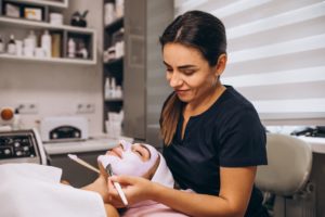 cosmetologist applying face mask on client