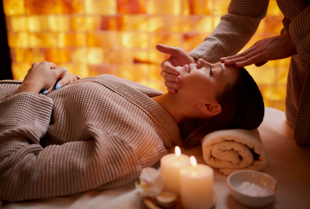 Woman lying on a massage table with candles while receiving a head massage
