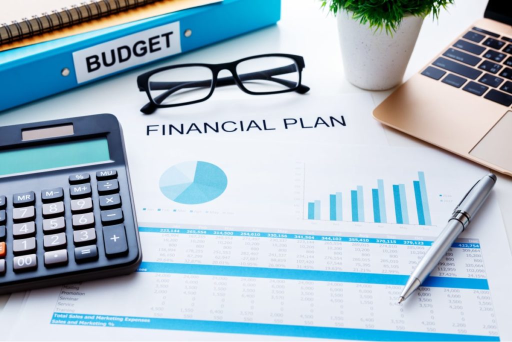 Close-up image of financial report, calculator, budget binder, and other various items on desk