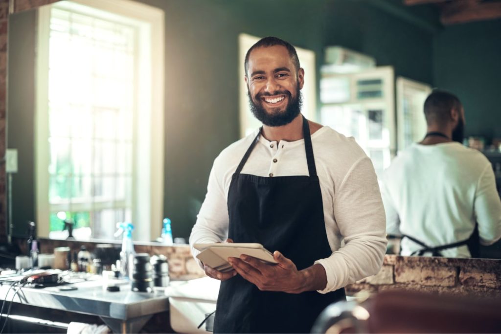 Man smiles while holding tablet in barbershop