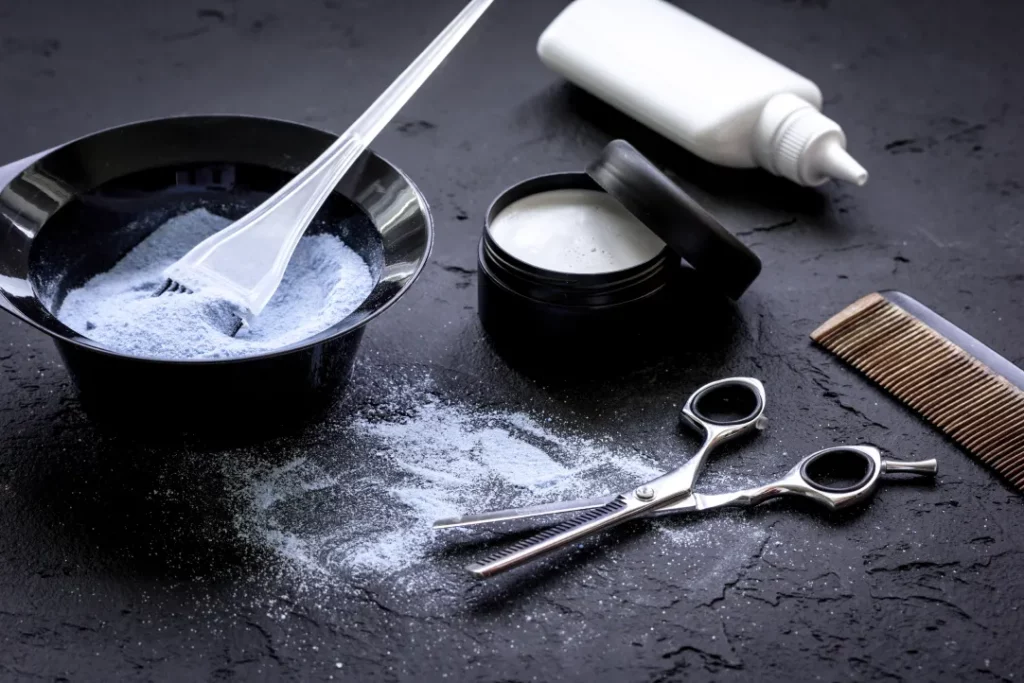 Developer, scissors, hair dye, a comb, and a squeeze bottle set atop a black salon counter.