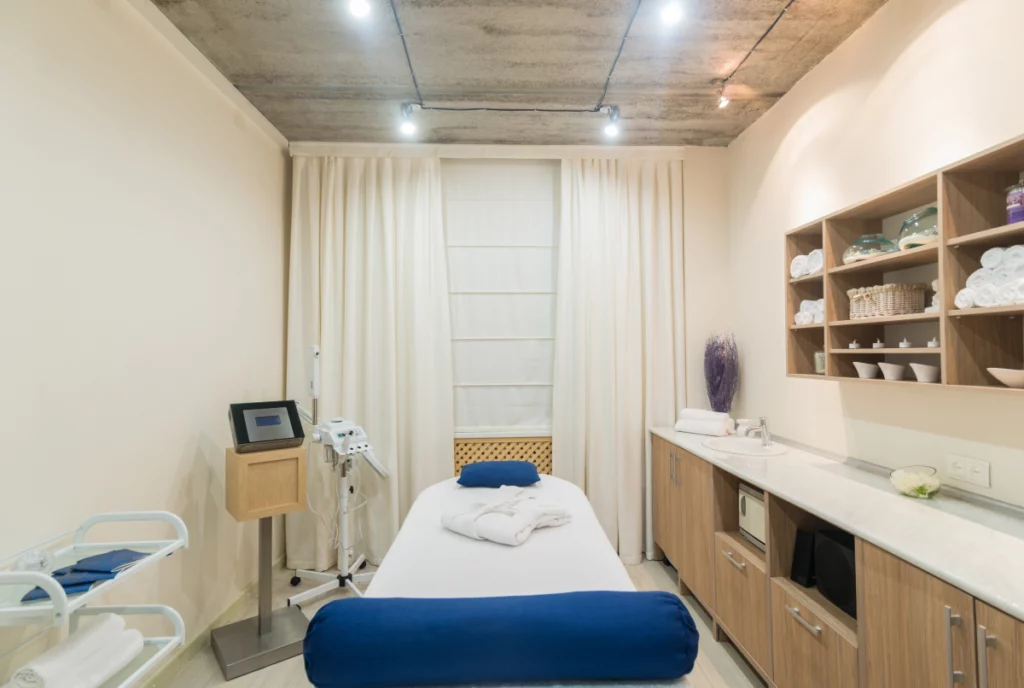 Interior of a small individual massage room with beige walls and blue pillows.