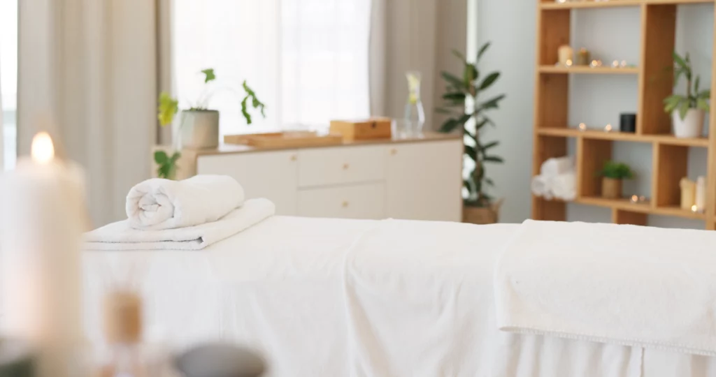 A massage room with a simple table covered in white sheets and a blurred spa background.