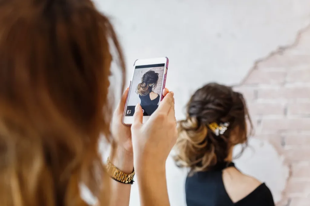 A hair stylist takes a photo of her client's hairstyle using a smartphone.