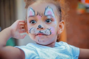 A young child with white and pink cat face paint.