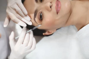 A med spa client smiles while receiving a Botox injection from a med spa professional wearing white gloves and holding a syringe.