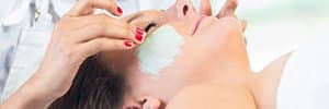 esthetician applying facial mask on clients cheeks
