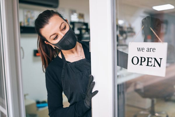 hairstylist with mask on hanging up we are open sign at salon