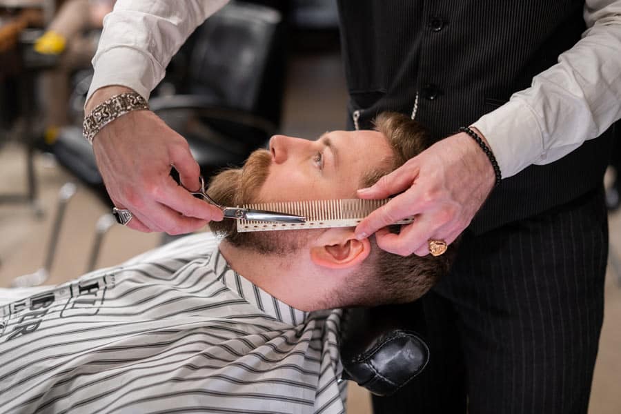 barber trimming a mans beard with scissors