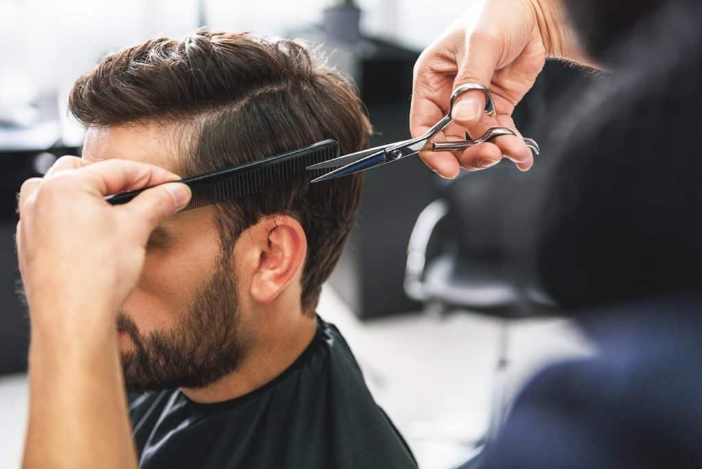 barber cutting mans hair with scissors and comb