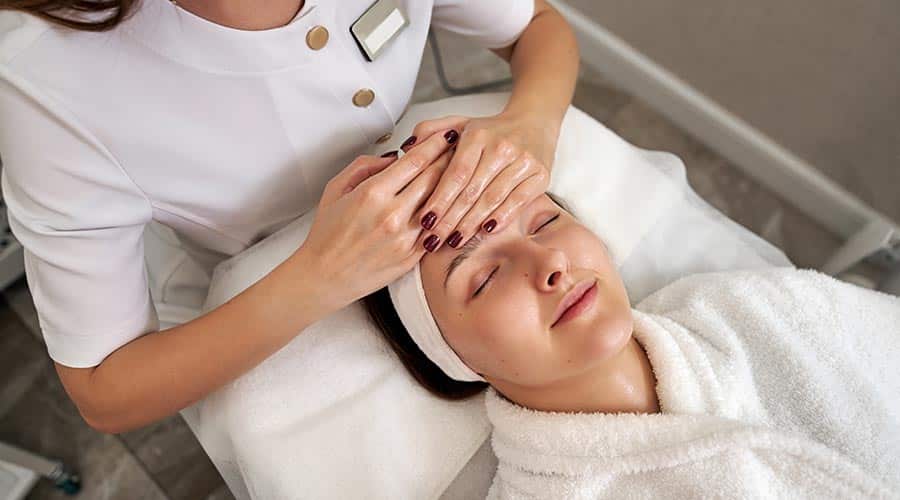 esthetician placing both hands on clients forehead during treatment